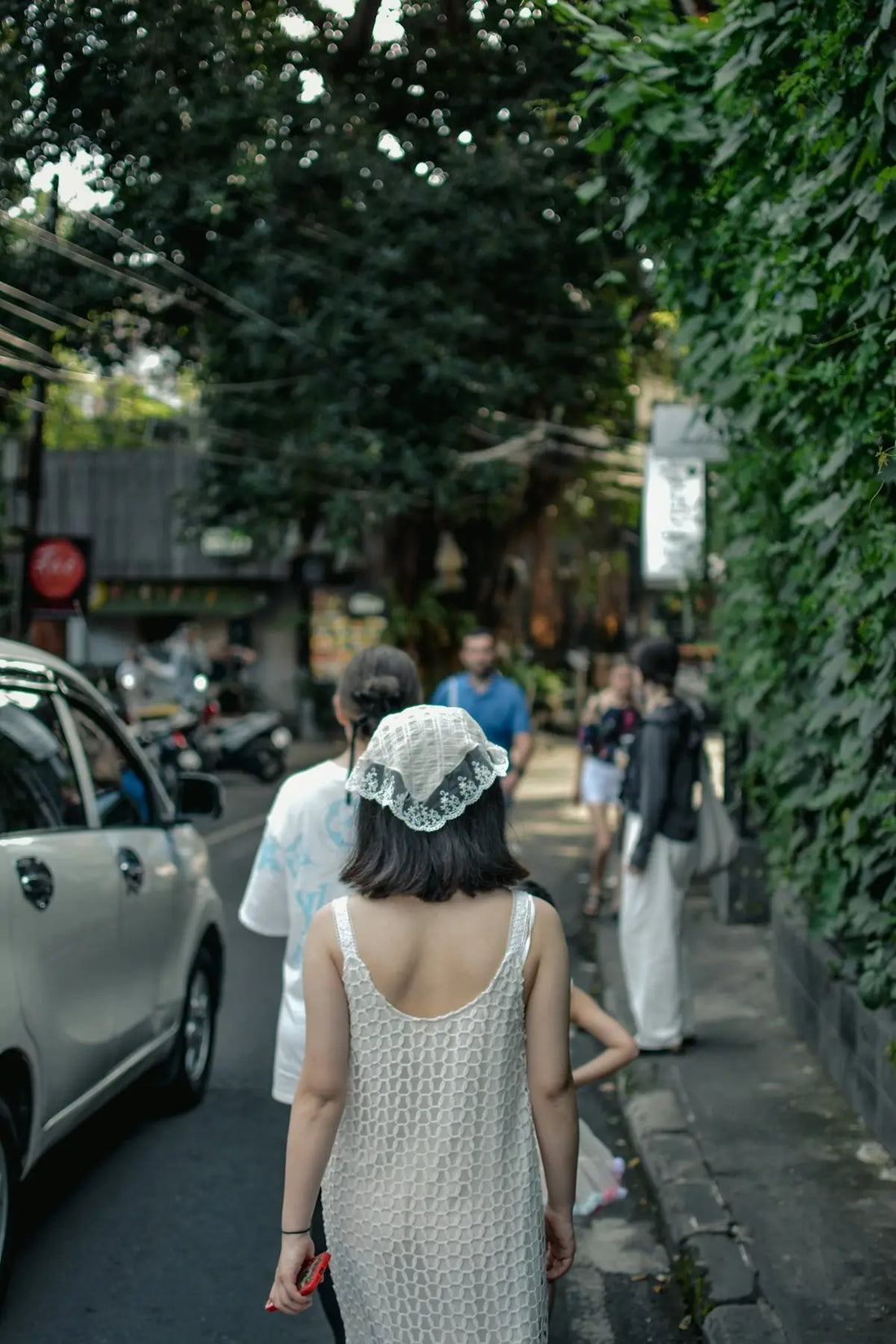 People walk down a street lined with greenery.