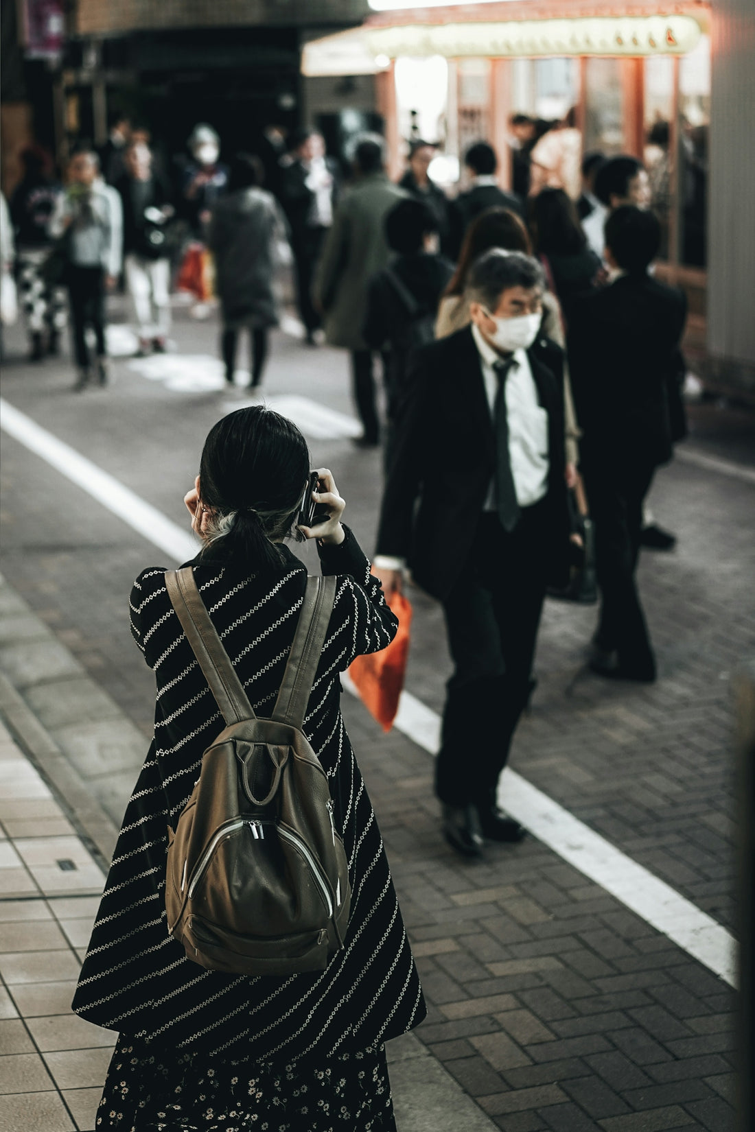 woman wearing black and white stripe coat using black smartphone while walking on street during daytime