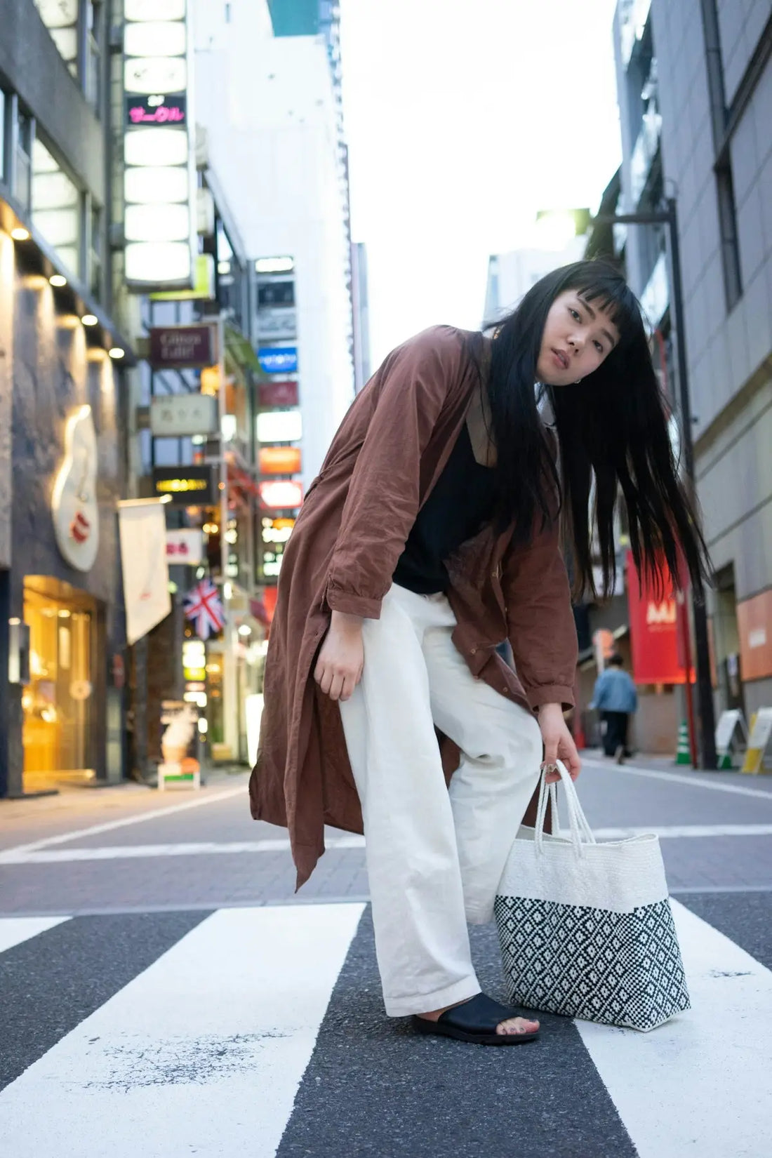 a woman standing on a cross walk holding a shopping bag
