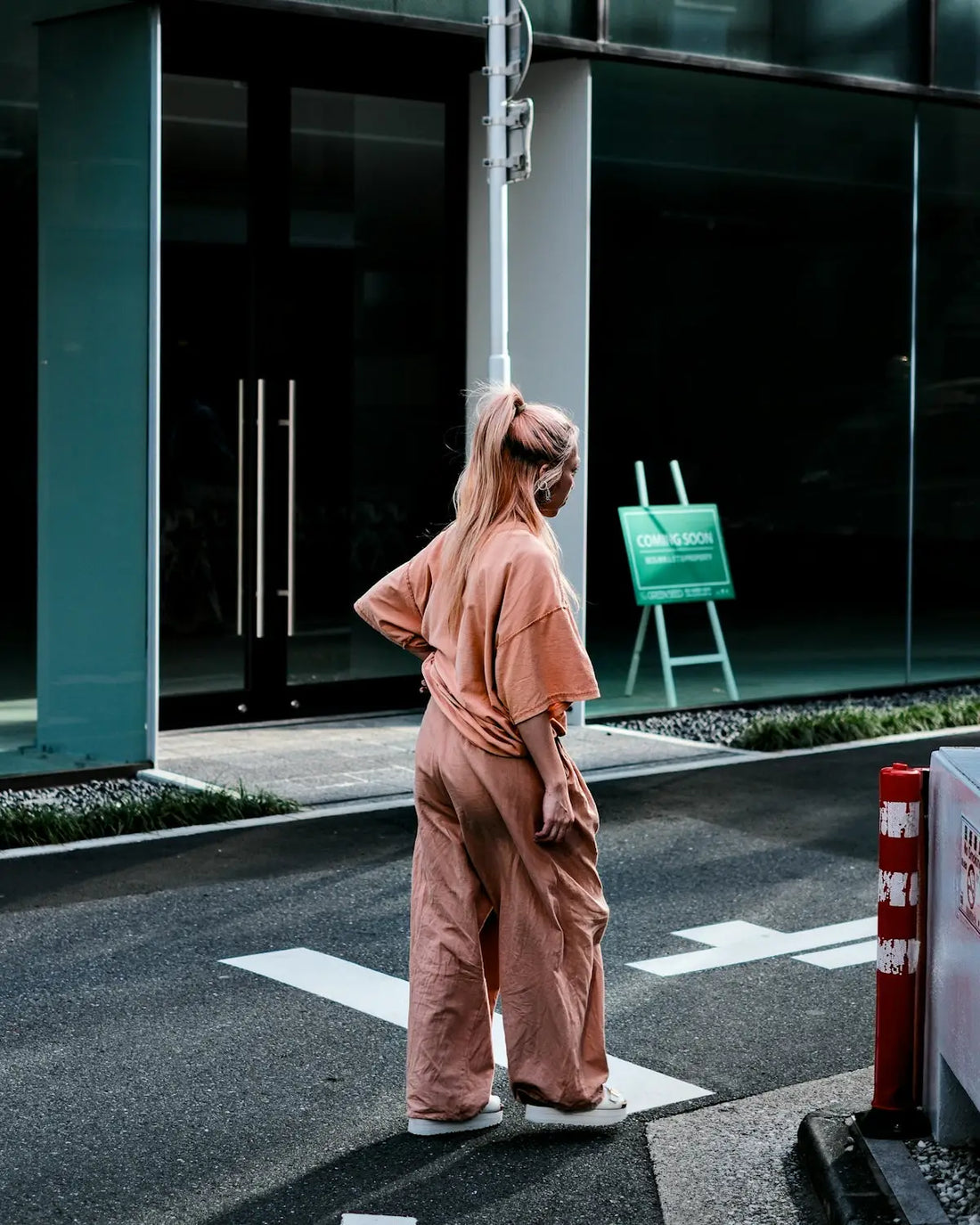 A woman in pink stands on a crosswalk.